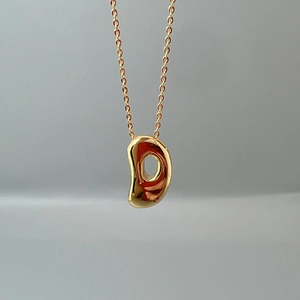 Macro shot of gold bean pendant on a fine O-chain necklace with smooth polished finish