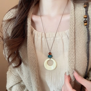 Vue détaillée d'un collier à pendentif géométrique en acrylique sur un pull beige