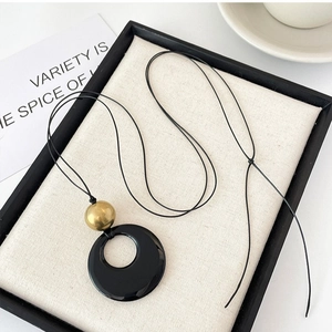 Minimalist necklace with a black round hollow pendant and golden bead on a black cord
