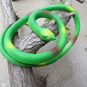 Serpent jouet en caoutchouc vert avec motifs jaunes sur une branche d'arbre