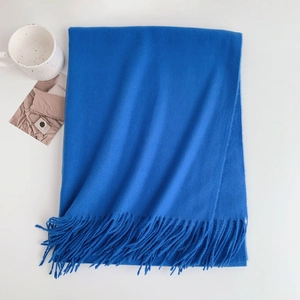 Flat lay of a soft blue cashmere-style scarf with tassel detail next to a white mug