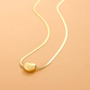 Close-up of polished gold heart pendant with sleek snake chain on a warm background