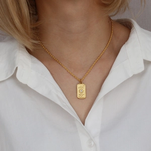 Detail shot of a gold tarot sun card pendant necklace on a model wearing white shirt
