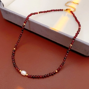 Detailed macro view of garnet beaded necklace with a central pearl and gold extension chain
