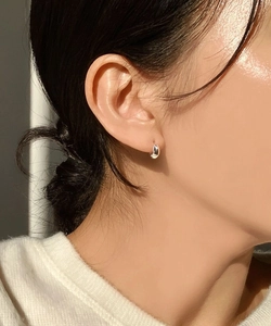 Close-up of minimalist oval sterling silver hoop earrings worn by a model in soft sunlight