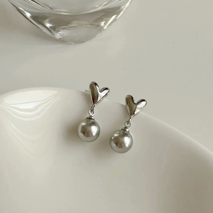 Elegant silver heart earrings with grey round pearls on a white ceramic plate