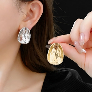 Detail of irregular oval metallic earrings with hammered texture in gold and silver finish