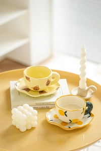 Close-up of wavy ceramic coffee cups with bear and lemon patterns on a saucer