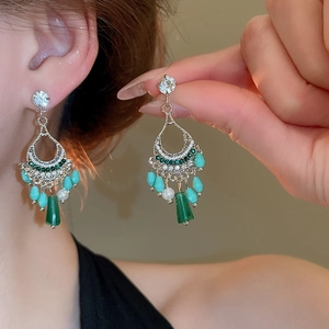 Close-up of vintage silver tassel earrings with green rhinestones and drop beads on model