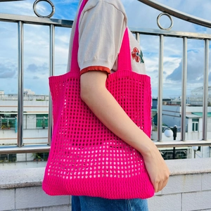 Detail of rose pink crochet knit tote bag with hollow out mesh pattern on a shoulder