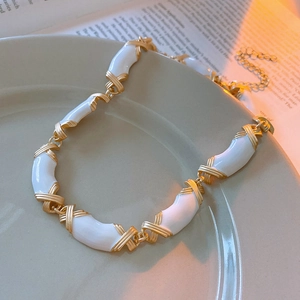Gros plan du collier vintage émaillé doré et blanc posé sur un plateau décoratif