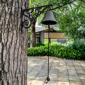 Vintage cast iron doorbell with scrollwork patterns on a tree trunk in a garden
