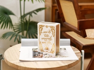 Detail of book-shaped white ceramic vase with gold text and quote on a wooden stand