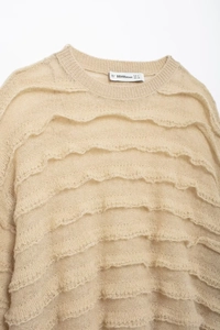 Macro shot of beige knit sweater showing delicate ruffle layers and fine fabric texture