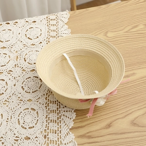 Détail d'un chapeau de paille enfant avec fleurs roses et cordon élastique sur dentelle