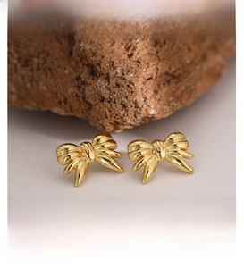 Macro detail of golden butterfly stud earrings with high-polish ribbon texture on rock