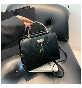 Détail d'un sac à main noir motif crocodile avec poignée en métal et breloque cerf