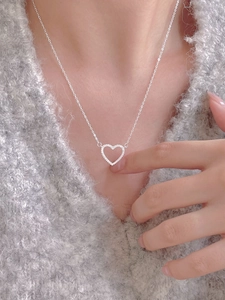 Close-up of a hollow heart necklace with pavé cubic zirconia worn on a grey sweater