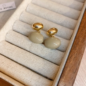 Gros plan de boucles d'oreilles en métal doré et résine beige dans un écrin à bijoux