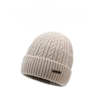 Macro detail of beige knit beanie showing thick cable knit texture and leather brand patch