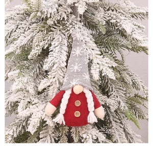 Close-up of knit Christmas gnome ornament with white braids hanging on a snowy tree