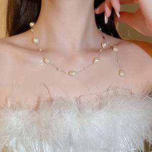Close-up of Baroque pearls and golden chain on a model wearing a white feather top