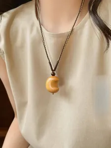 Close-up of wooden crescent moon pendant with woven rope on a beige linen shirt