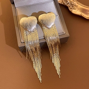 Elegant gold-tone heart studs with long chain tassels on a dark jewelry display box