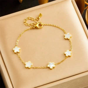 Gold-plated clover charm bracelet with white shell inlays on a jewelry cushion