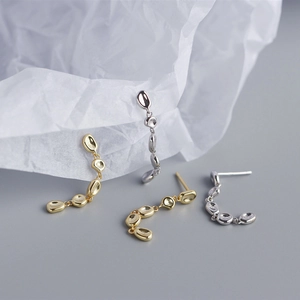 Close-up of gold and silver irregular pebble tassel drop earrings on textured paper
