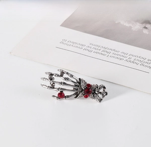 Detailed view of punk skull hand brooch with red rhinestones and antique silver finish