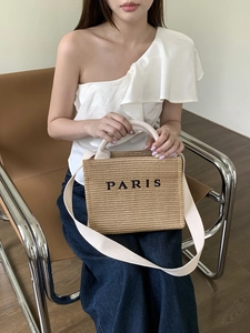 Chic khaki woven straw tote bag with wide white strap and Paris print on a seated model