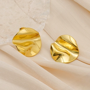 Détail macro de boucles d'oreilles disques dorés irréguliers sur tissu en soie plissée