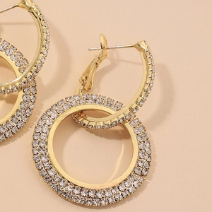 Elegant gold geometric circle earrings with dense rhinestone pavé on a beige background
