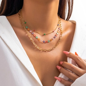 Close-up of three-layered gold necklace with colorful beads and floral charms on a model