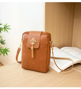 Detail of brown embossed cell phone bag with golden crown charm and tassel on a desk