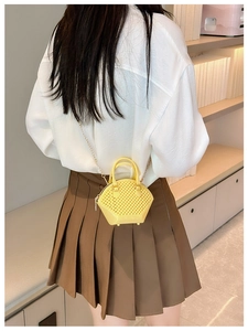 Detail of yellow mini shell bag with quilted texture and gold chain strap on model