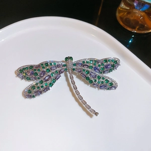 Detail van de libelbroche met groene en paarse kristallen op een wit keramisch bord