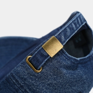 Close-up of adjustable bronze buckle and strap on blue denim baseball cap detail