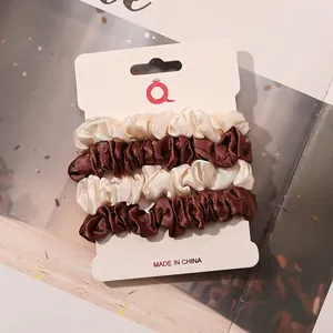 Detail of four satin scrunchies in cream and dark brown on a white display card