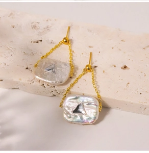 Close-up of baroque pearl earrings with gold chains and square crystal pendants
