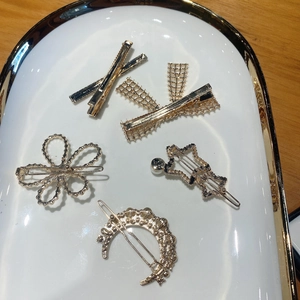 Detailed view of assorted gold alloy hair clips with pearls on a white ceramic tray