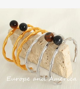 Detail of bamboo joint open bangles in gold and silver with spherical tiger eye gemstones