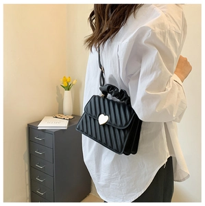 Detail of black pleated handbag with V-shaped texture, golden heart buckle and ruffled handle