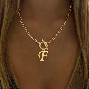 Close-up of golden paperclip chain necklace with letter F and ring pendant on model