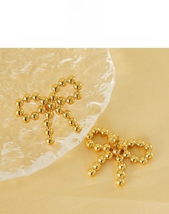 Detailed shot of 18K gold beaded bow earrings on a textured glass surface