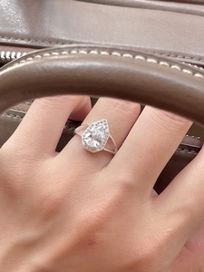 Macro shot of silver pear-shaped halo ring with side accent diamonds on a leather bag