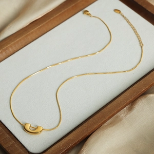 Élégant collier chaîne serpent dorée avec pendentif en U minimaliste sur feutre gris