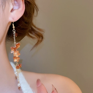 Close-up of translucent orange flower resin beads and white pearls on long gold tassels