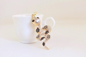 Close-up of golden snake keychain pendant with sparkling rhinestones on a white cup